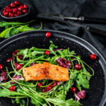 Seafood salad with salmon, arugula, lettuce and cranberries. Black background. Top view